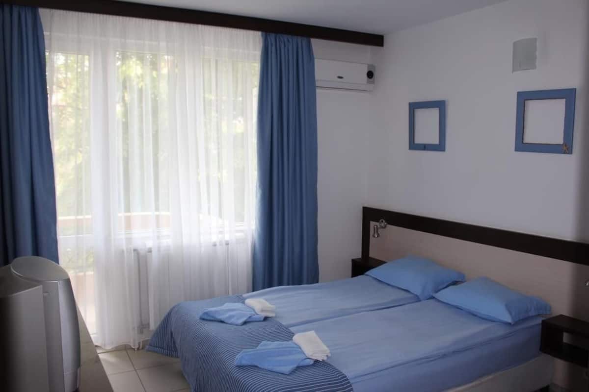 Ein Hotelzimmer mit zwei Betten, einem Fernseher und einem Fenster mit Vorhängen.