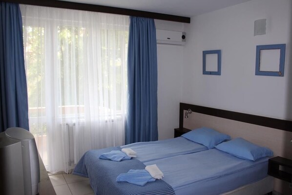 A hotel room with two beds, a TV, and a window with curtains.