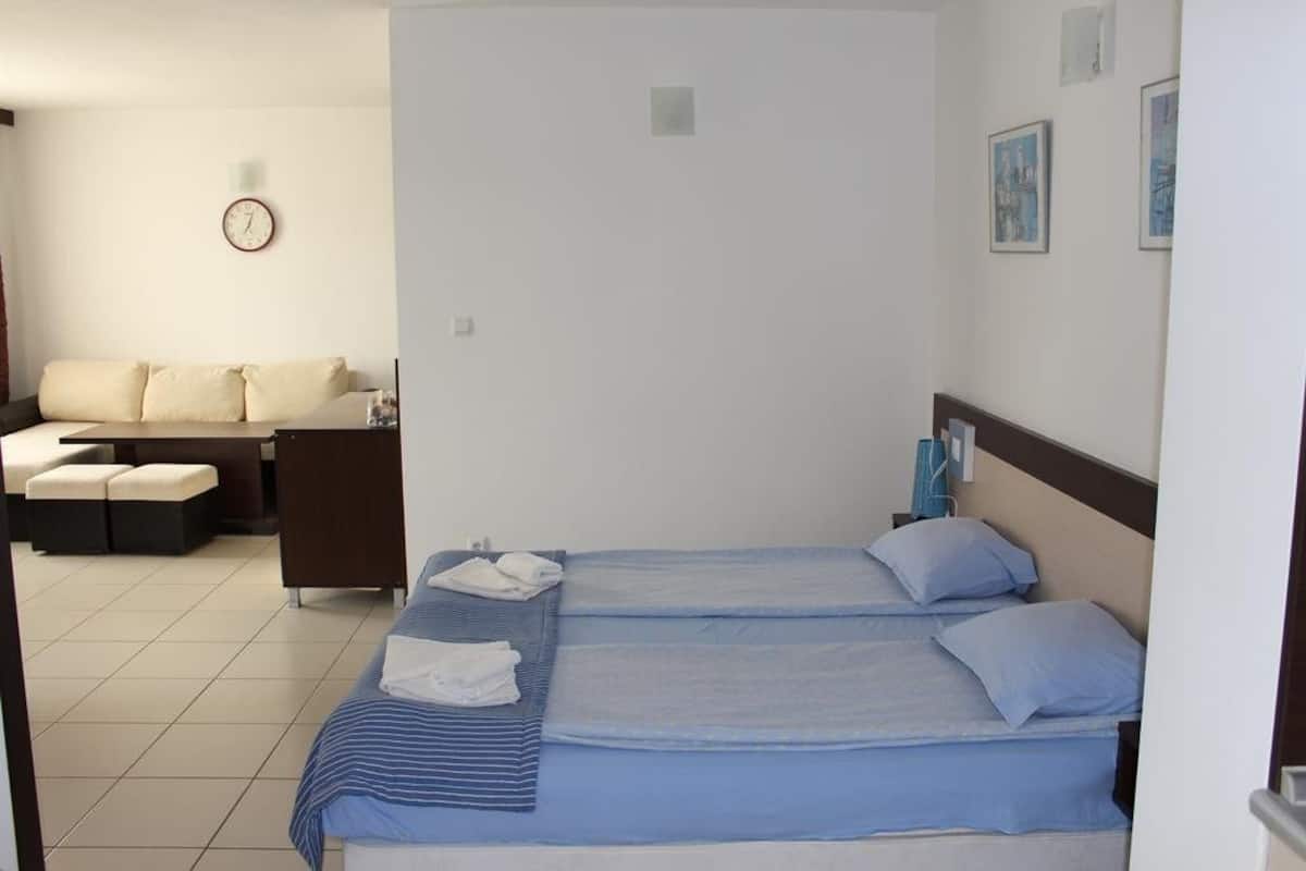 Ein Hotelzimmer mit zwei Betten, einer Sofagarnitur, einem Schreibtisch und einer Uhr an der Wand.