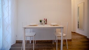 A dining area with a white table set for two, two white chairs, and a small side table with condiments. - Rebecca's House (Verona)