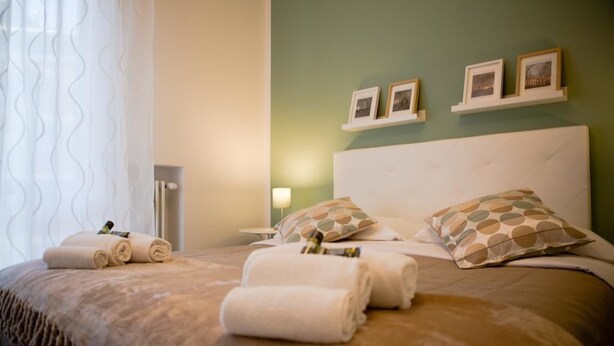 A hotel room with a large bed, neatly folded towels, and a wall with three framed pictures. - Rebecca's House (Verona)
