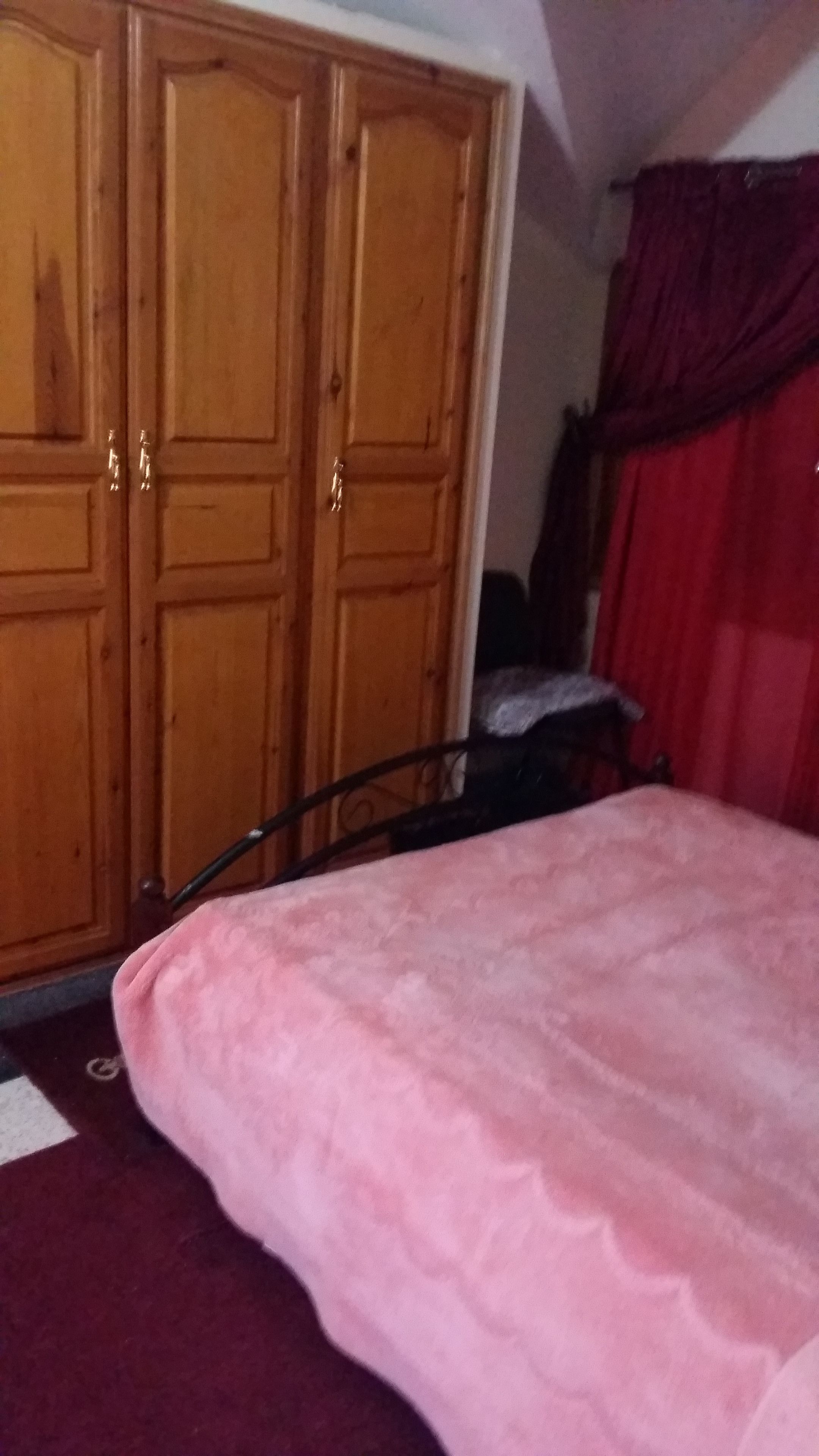 Un dormitorio con un armario de madera, una cama con colcha rosa y una cortina roja.
