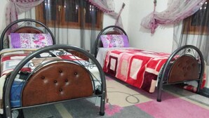 A room with two metal-framed beds with wooden headboards, each with a floral-patterned pillow. The room has a tiled floor with a pink and grey rug. - Sweet Azrou Holiday (Azrou)