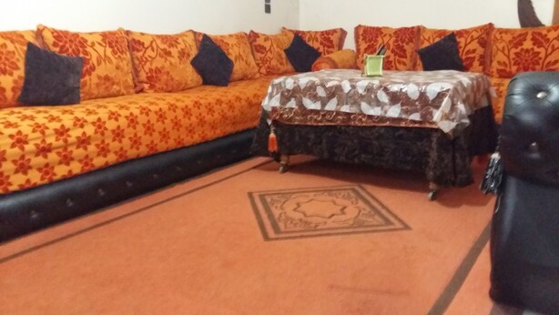 Un salón con sofá, reposapiés y una mesita con mantel estampado.