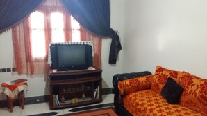 A living room with a television on a wooden stand, a sofa with floral cushions, and a small table with a cloth. - Sweet Azrou Holiday (Azrou)