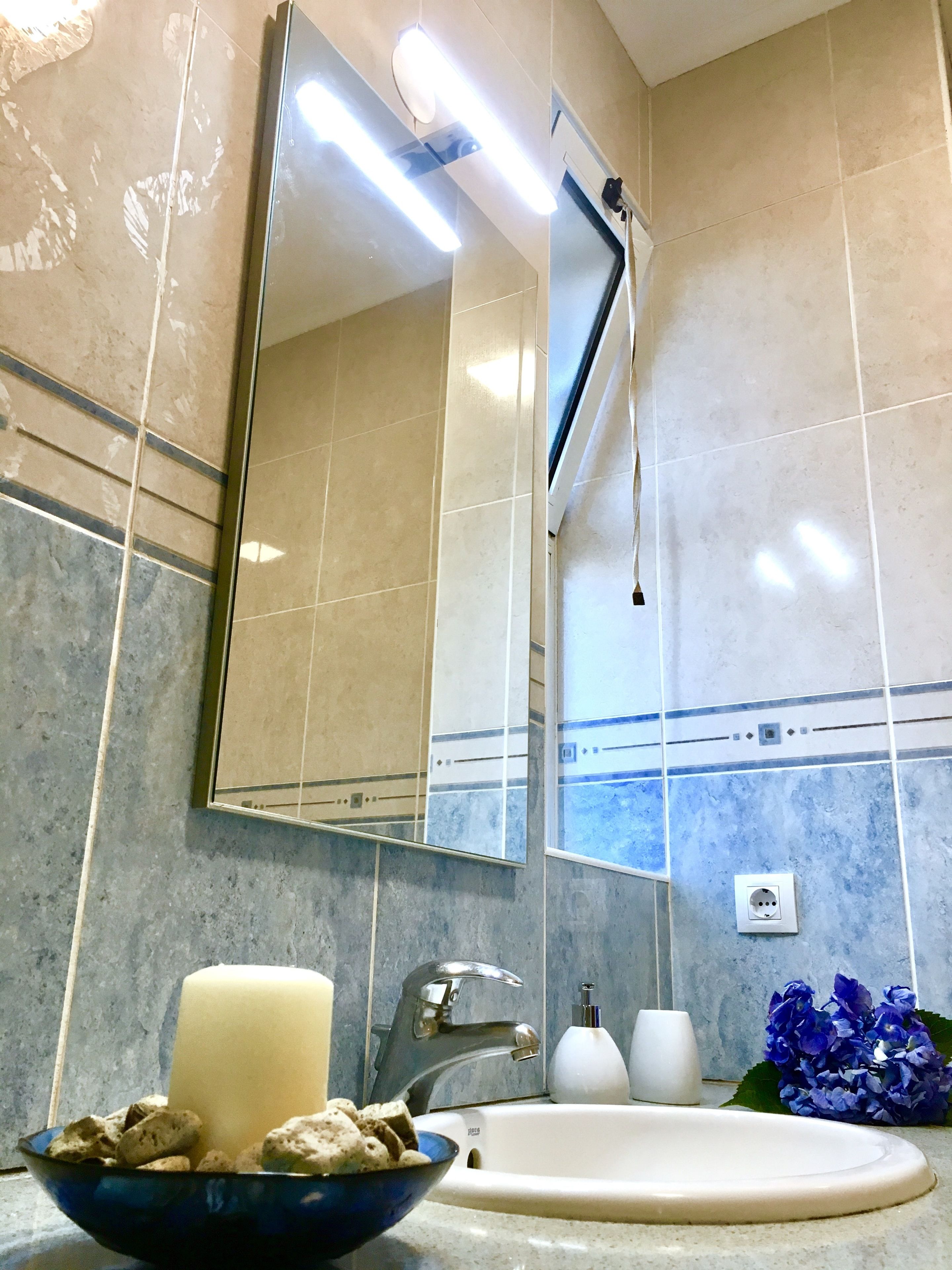 A bathroom with a large mirror, a sink, a towel rack, and a wall-mounted light fixture.