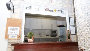 A kitchen with grey cabinets, a microwave, and a sink. There is a corkboard with a notice and a potted plant on the counter.