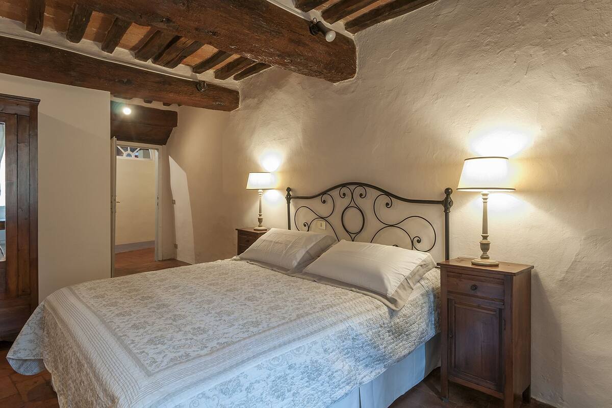 A bedroom with a bed, two bedside lamps, a wooden nightstand, and a rustic ceiling.