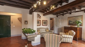 A cozy living room with a stone fireplace, striped armchairs, a wooden cabinet, and a staircase leading upstairs. - B&B Arena di Lucca (Lucca)