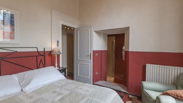Un dormitorio con una cama, una mesita de noche, una silla, una puerta que da a un baño y un radiador.