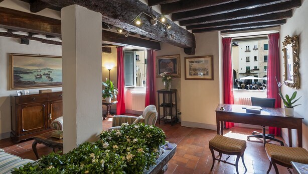 A cozy room with a wooden ceiling, a dining table, chairs, a sofa, a potted plant, and artwork on the walls. - B&B Arena di Lucca (Lucca)