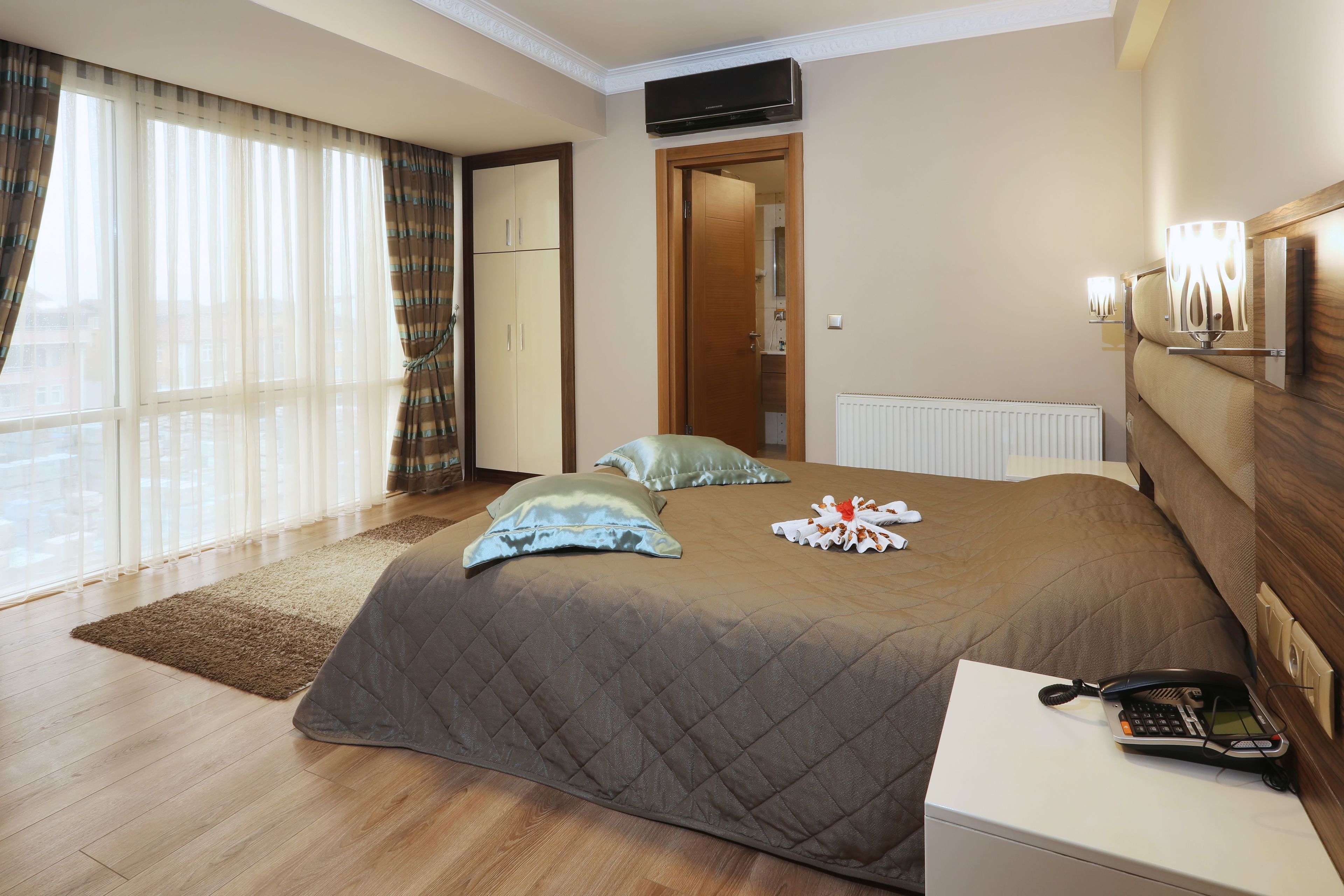 Una habitación de hotel con una cama grande, un teléfono en la mesita de noche y vistas de la ciudad por la ventana.