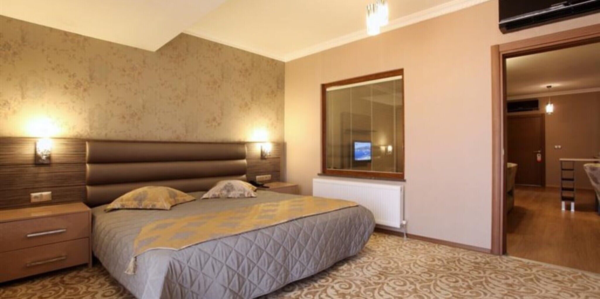 Un dormitorio con cama, mesitas de noche, un espejo grande y televisor.
