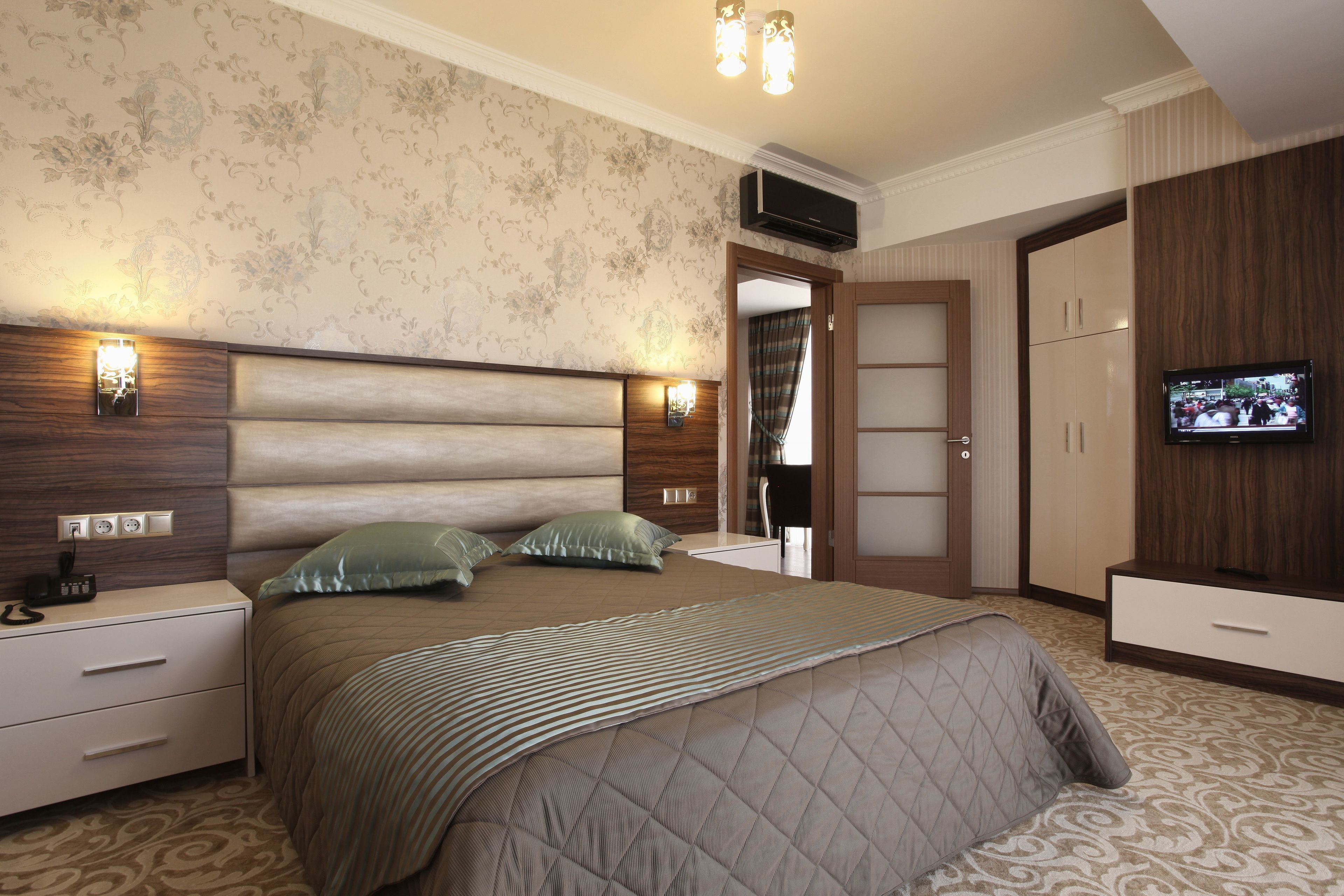 A bedroom with a large bed, bedside tables, a TV, and a wardrobe.