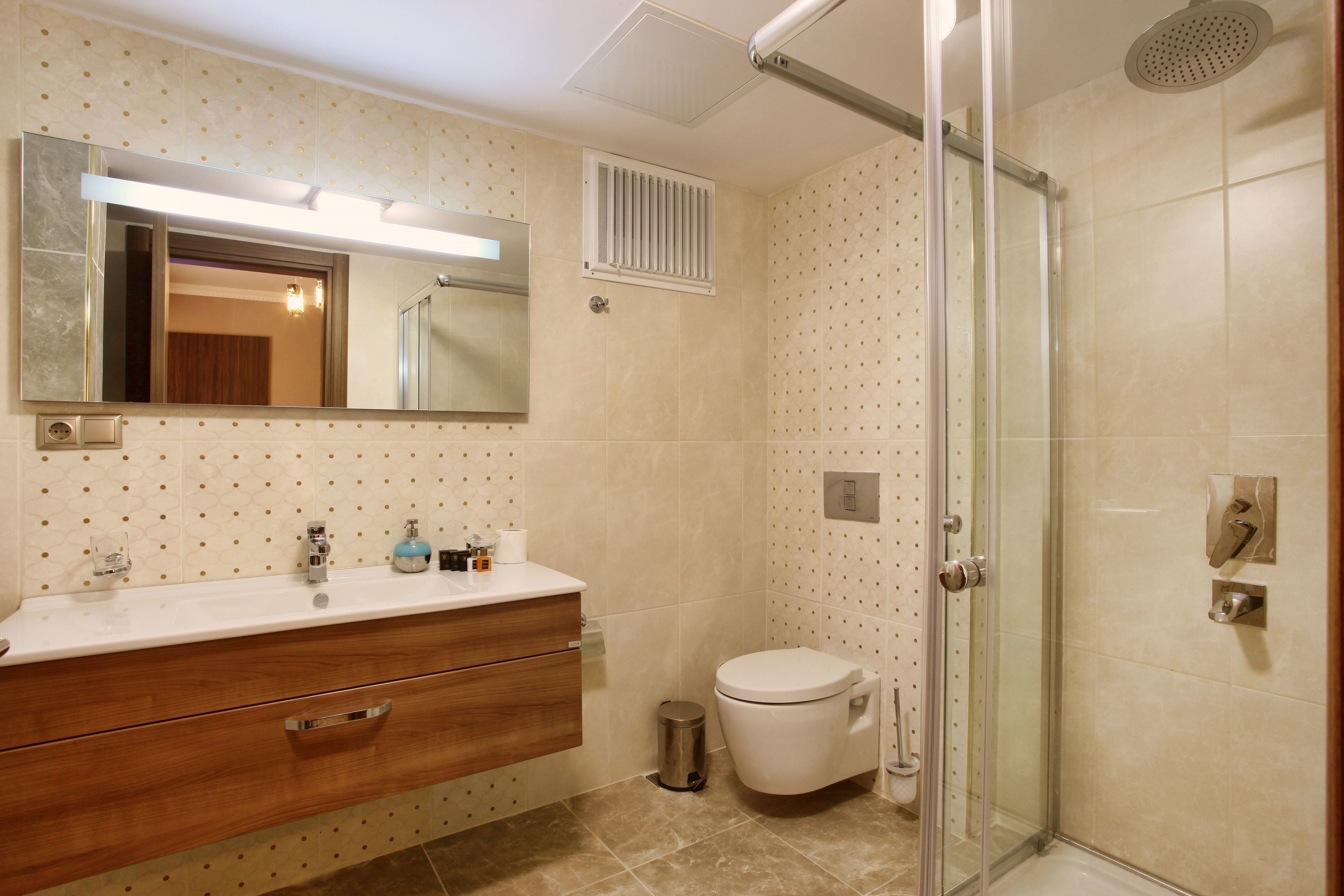 Un baño con tocador de madera, inodoro, ducha con puerta de cristal y espejo con luz superior.