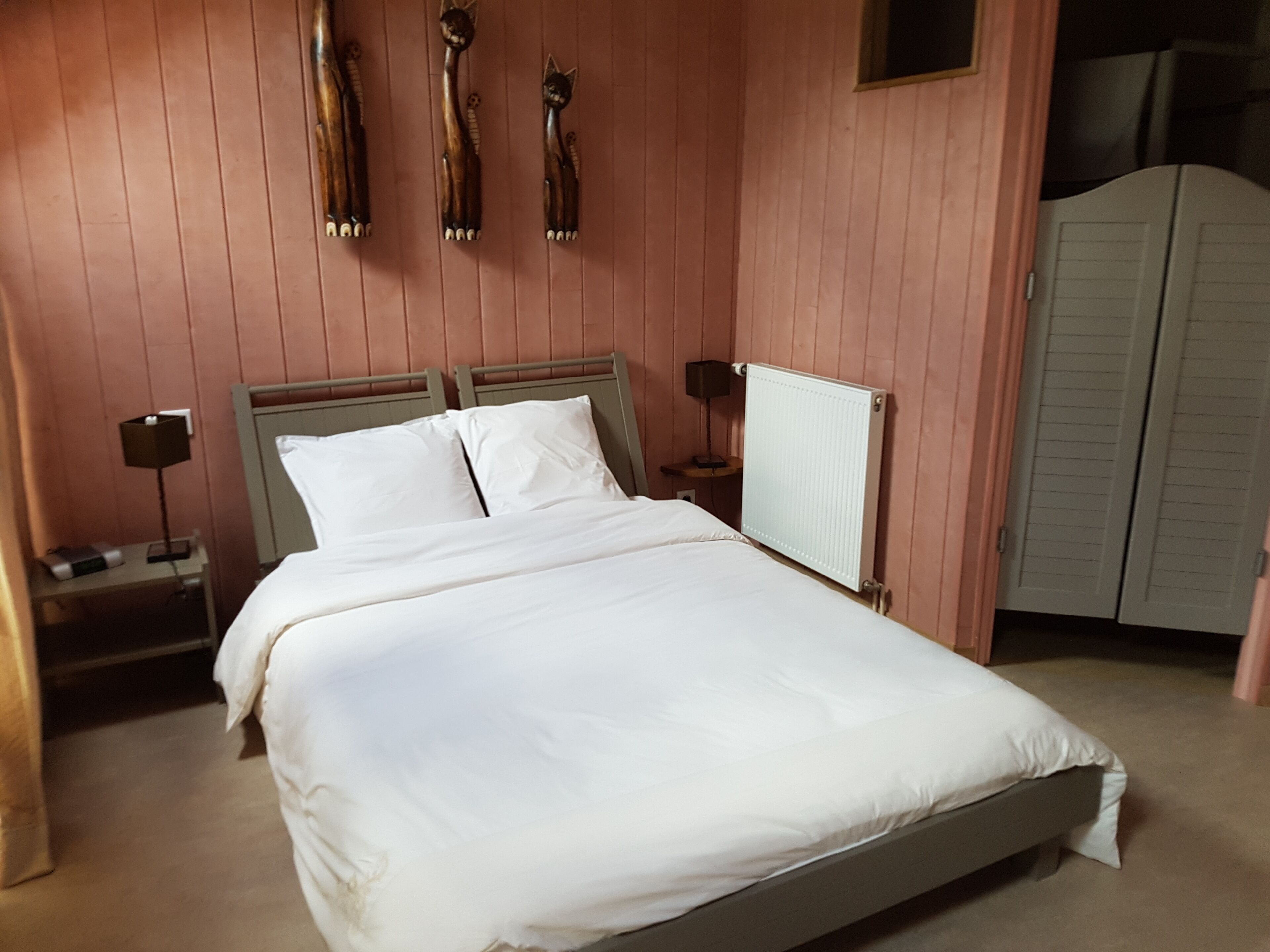 A bedroom with a bed, two bedside tables, a nightstand, a radiator, and a wardrobe.