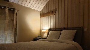 A bedroom with a wooden headboard, a bedside table with a lamp, and a bed with a beige blanket. - Relais des Caillères (Saint-Pavace)