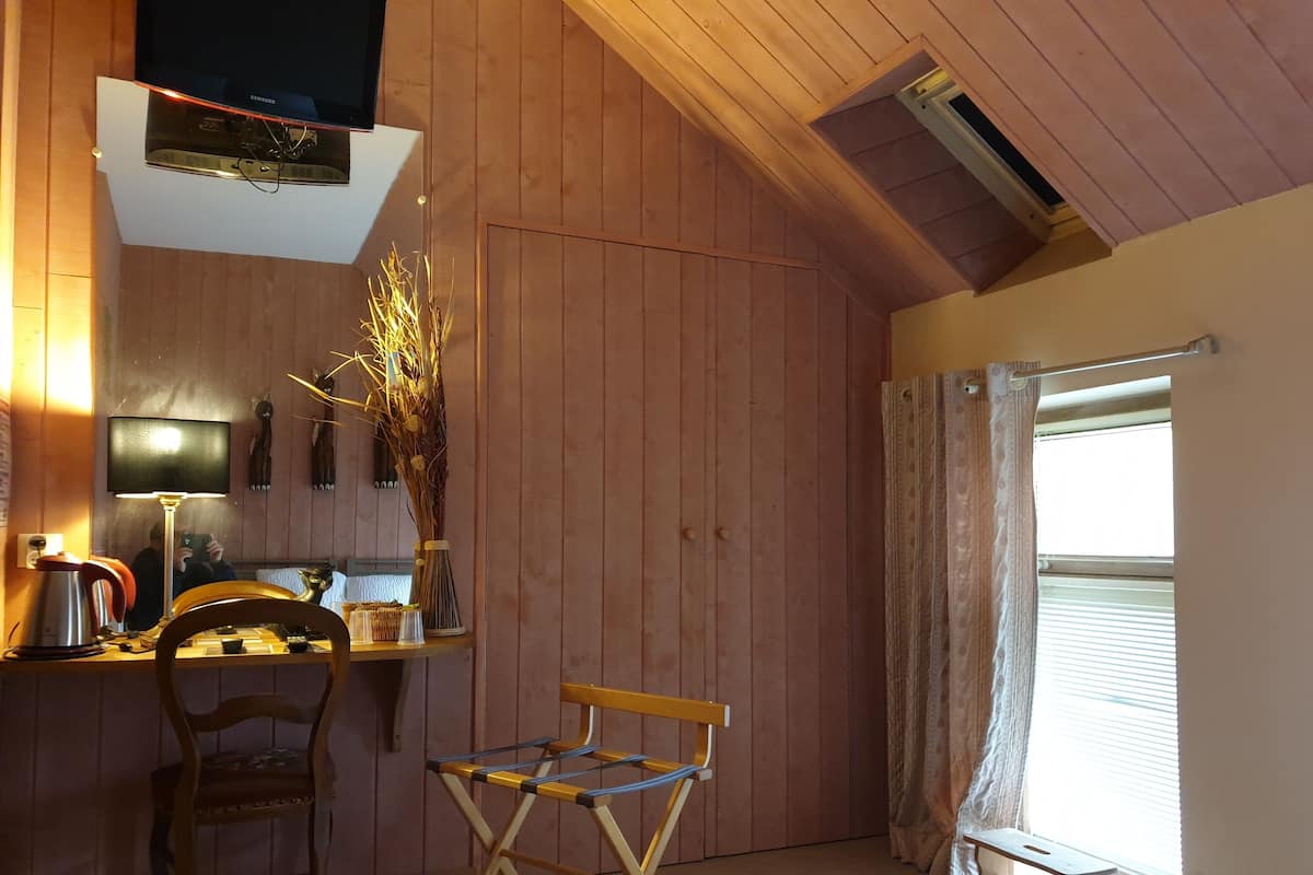 Une pièce chaleureuse avec des murs en bois, un bureau avec une lampe, une chaise, un lit et une fenêtre avec des rideaux.