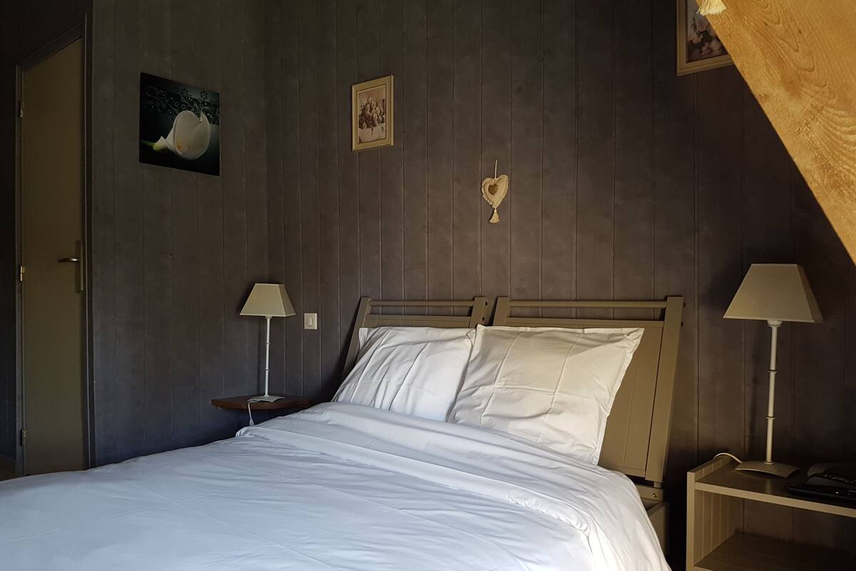 Une chambre à coucher avec une tête de lit en bois, deux tables de chevet avec des lampes, un lit avec une literie blanche et un luminaire fixé au mur.