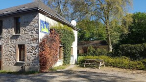 A stone building with a flag, a picnic table, and a gravel driveway. - Relais des Caillères (Saint-Pavace)