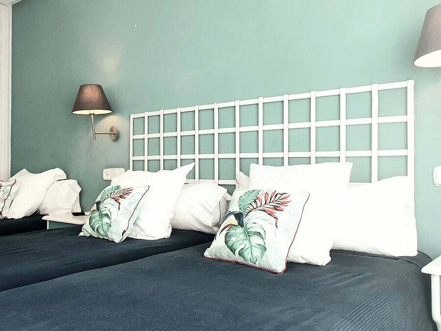 Une chambre avec deux lits, une armoire blanche, une table de chevet avec une lampe et un thermostat fixé au mur.