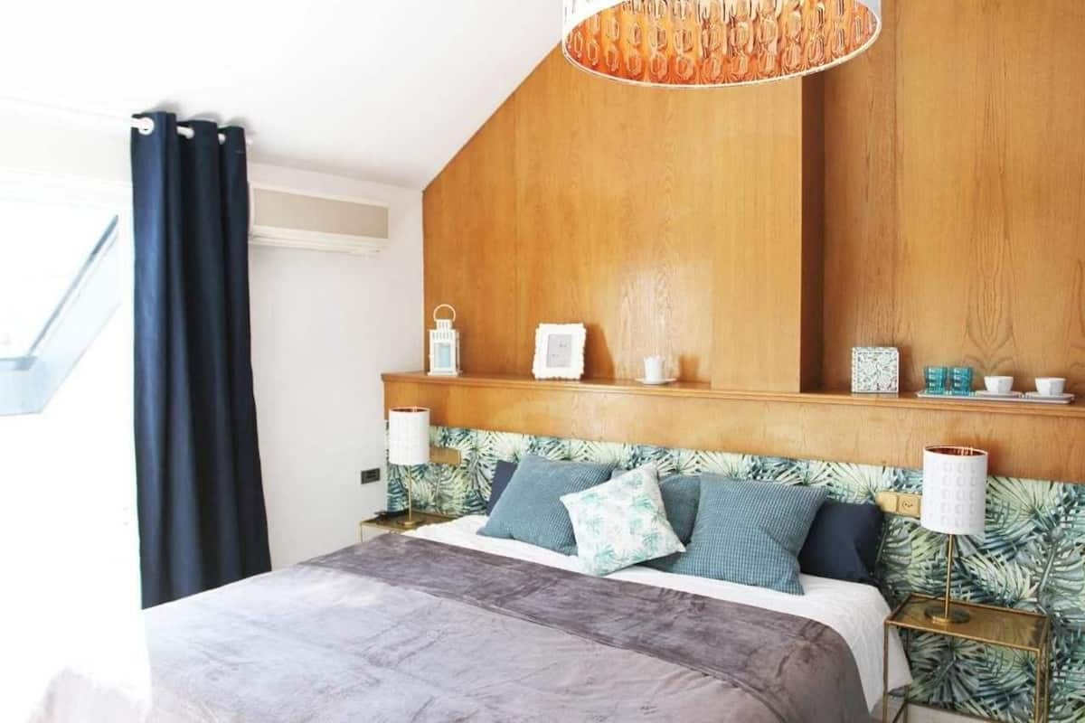 Une chambre à coucher avec une tête de lit en bois, un lit recouvert d’une couvre-lit grise et une table de chevet avec une lampe.