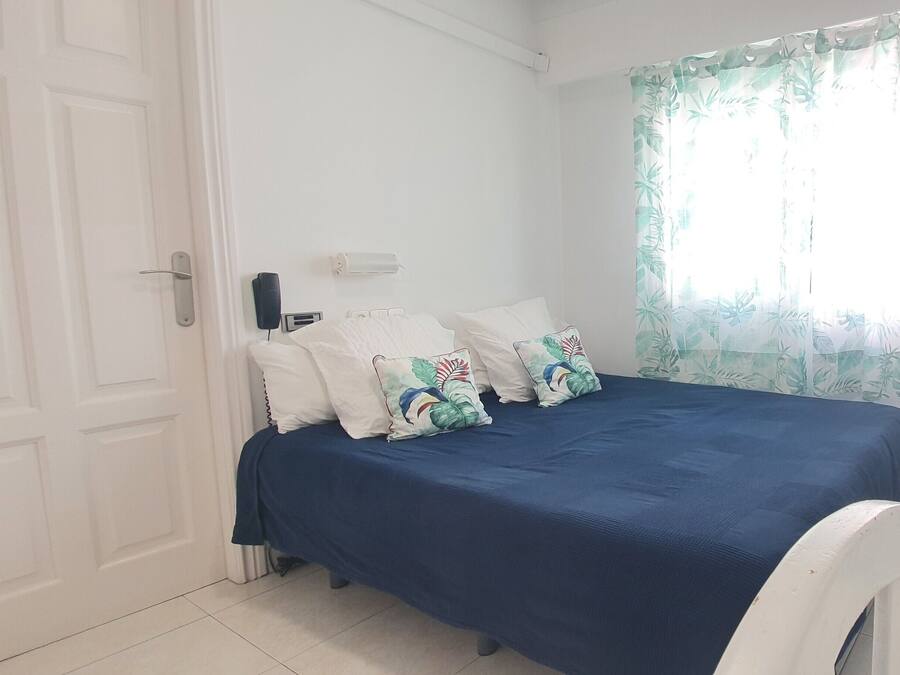 Un dormitorio con cama, almohadas, una ventana con cortina floral y una puerta blanca.