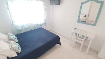 Una camera da letto con un letto, una sedia, una finestra con tenda, uno specchio e un televisore fissato al muro.