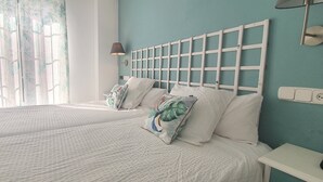 Un dormitorio con dos camas, una ventana con cortinas, una mesita de noche y una lámpara de pared.