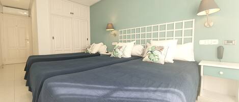 Una habitación con dos camas, un armario blanco, una mesita de noche y una lámpara de pared.