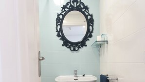 Un baño con un lavamanos blanco, un espejo negro ornamentado y un taburete blanco pequeño.