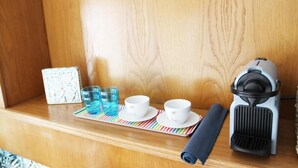Una estantería de madera con una cafetera, dos tazas blancas, un vaso azul y un posavasos a rayas.