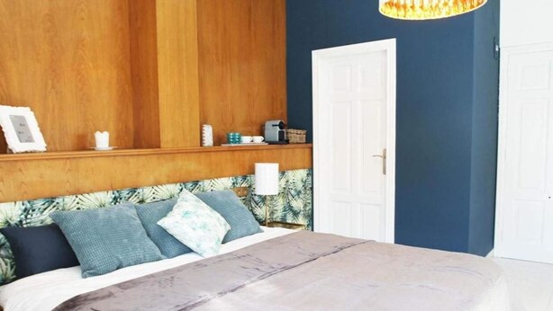 Un dormitorio con cabecera de madera, cama con colcha gris y mesita de noche con lámpara.