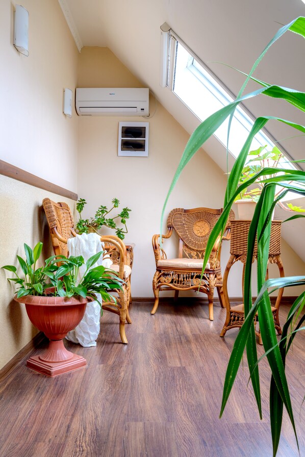 A room with two wicker chairs, a red pot with green plants, and a window with natural light.