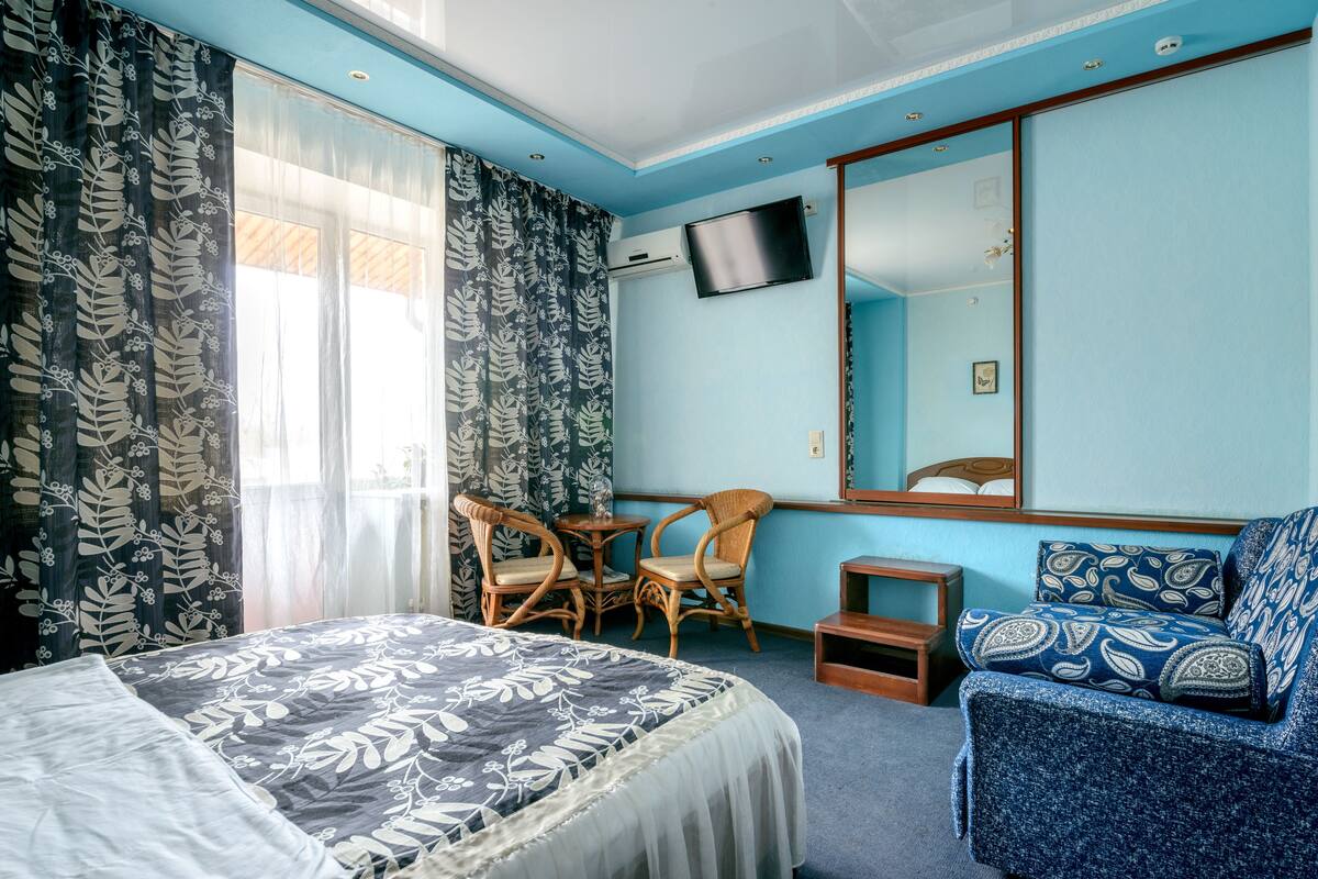 A hotel room with a bed, a chair, a small table, a sofa, a TV, and a mirror.