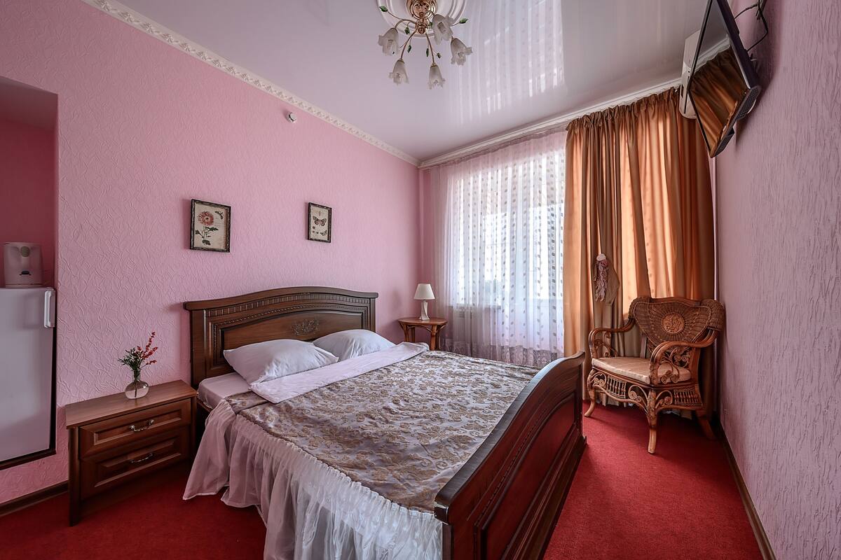 A bedroom with a wooden bed, a nightstand, a chair, a ceiling fan, and a window with curtains.
