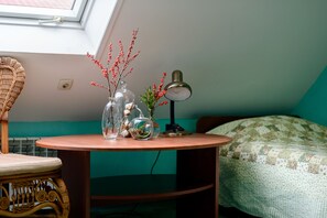 A small round table with a lamp, a wicker chair, and a bed with a quilt.