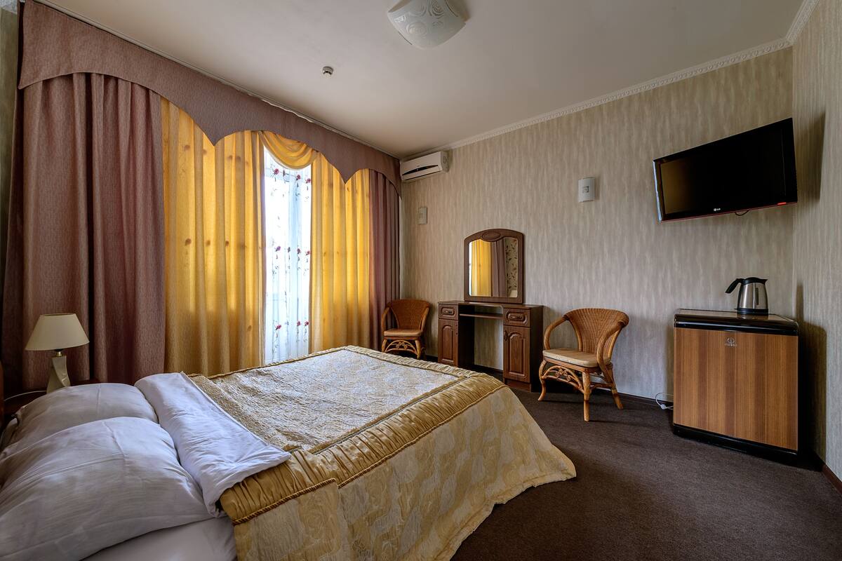 A hotel room with a bed, two chairs, a desk, a television, and a wardrobe.
