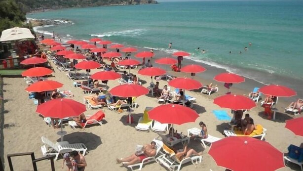 A beach with numerous red umbrellas and white lounge chairs.