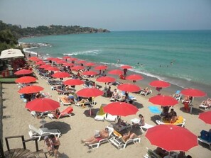 Una playa con numerosas sombrillas rojas y sillas de playa blancas.