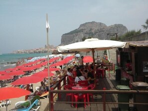 Un restaurante frente a la playa con sombrillas rojas y mesas al aire libre.