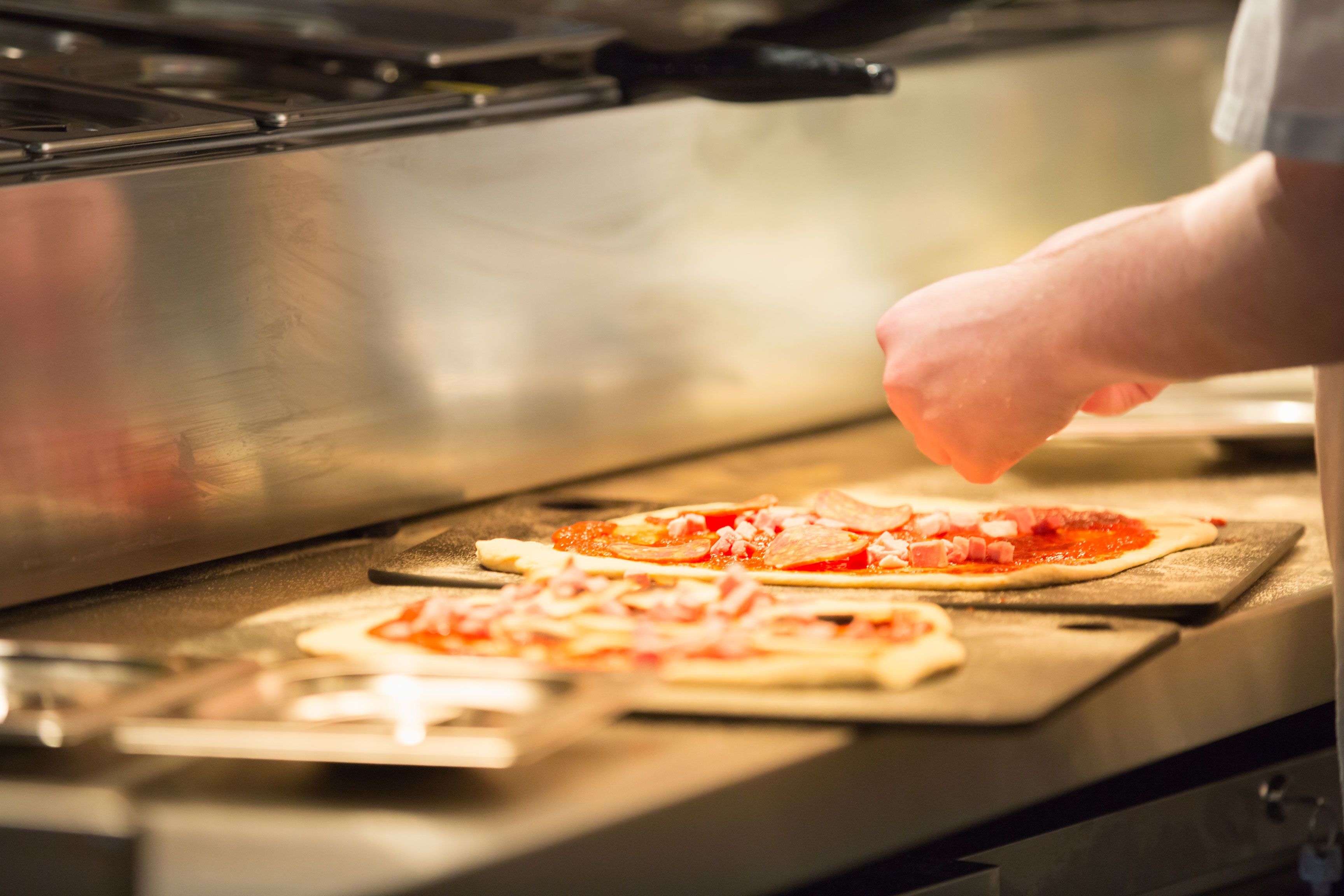 Een keuken met een roestvrijstalen oven en een persoon die pizza's bereidt op houten snijplanken.