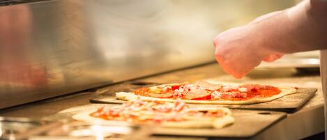 Een keuken met een roestvrijstalen oven en een persoon die pizza's bereidt op houten snijplanken.