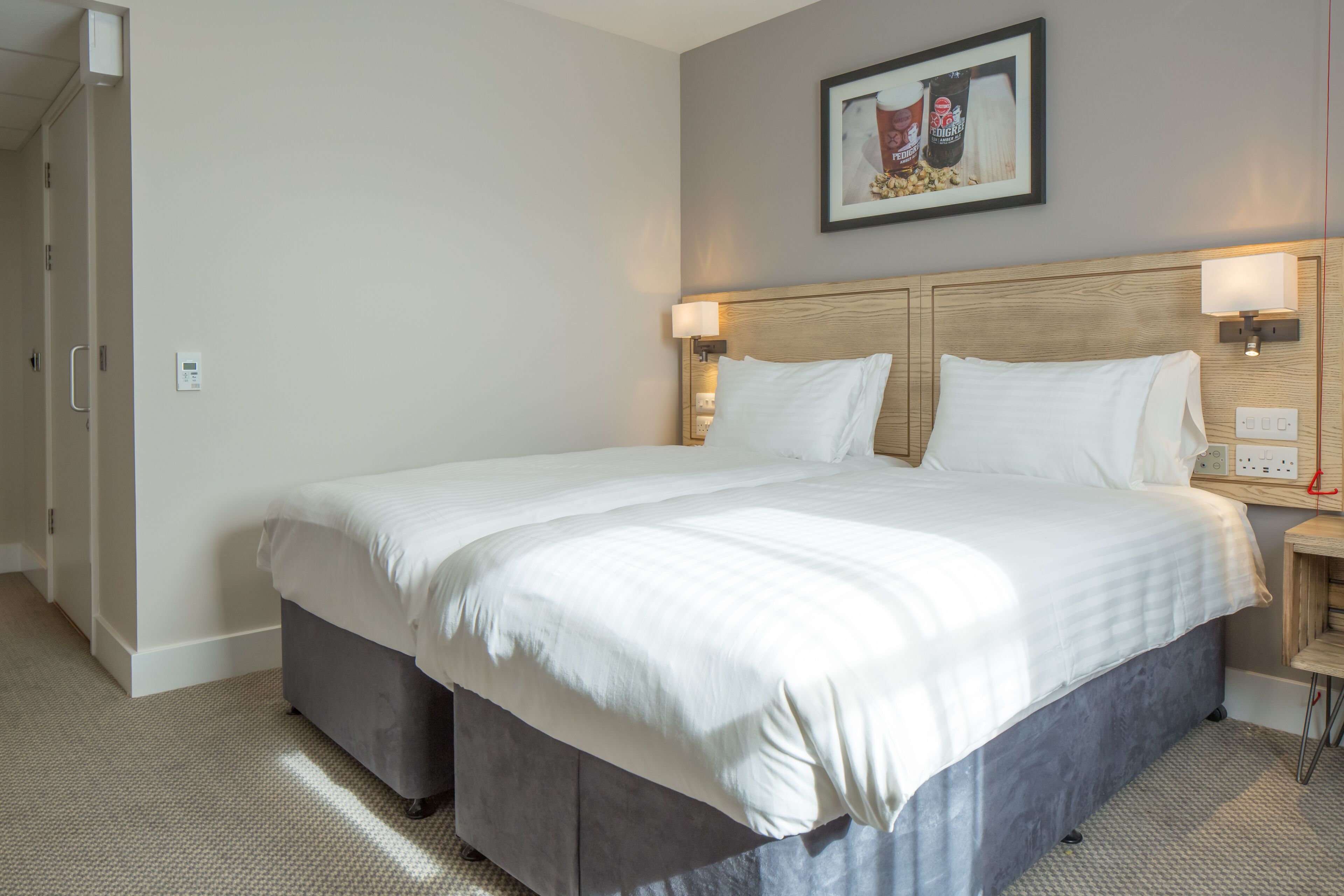 A neatly made bed in a hotel room with a headboard, bedside lamps, and a wall-mounted light fixture.