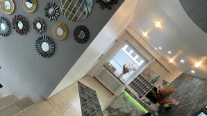 Een modern interieur met een trap, decoratieve spiegels en een zithoek met een groene stoel.