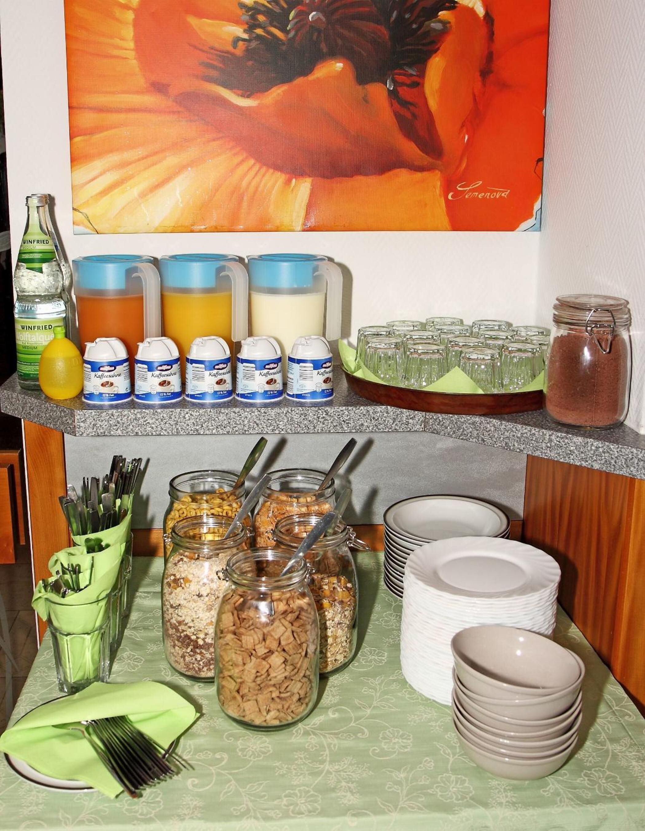 Una barra de desayuno con diversos alimentos y bebidas, incluyendo botes de cereal, leche y café, además de una botella de zumo de naranja.