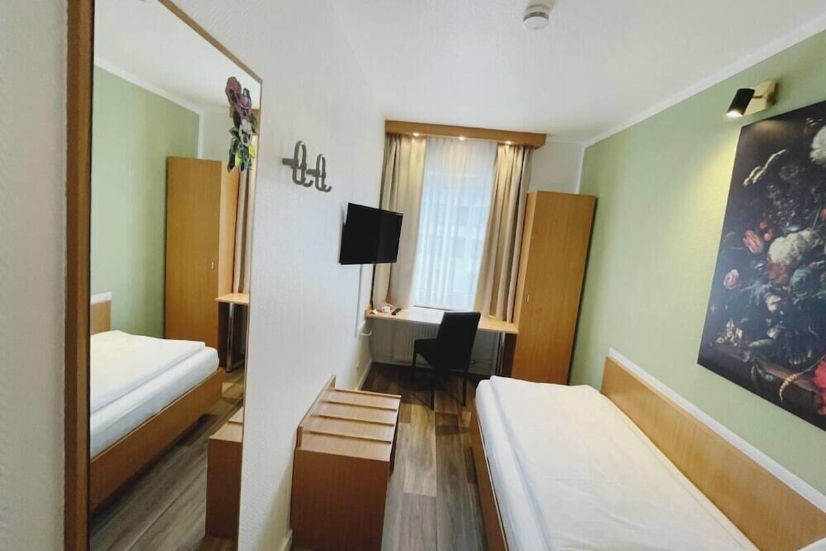 Ett hotellrum med två separata sängar, ett skrivbord, en stol, en tv och en tavla på väggen.
