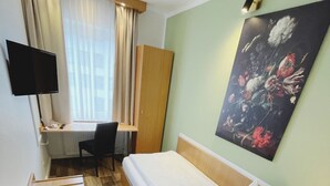 Een hotelkamer met een bed, bureau, stoel en een schilderij aan de muur.