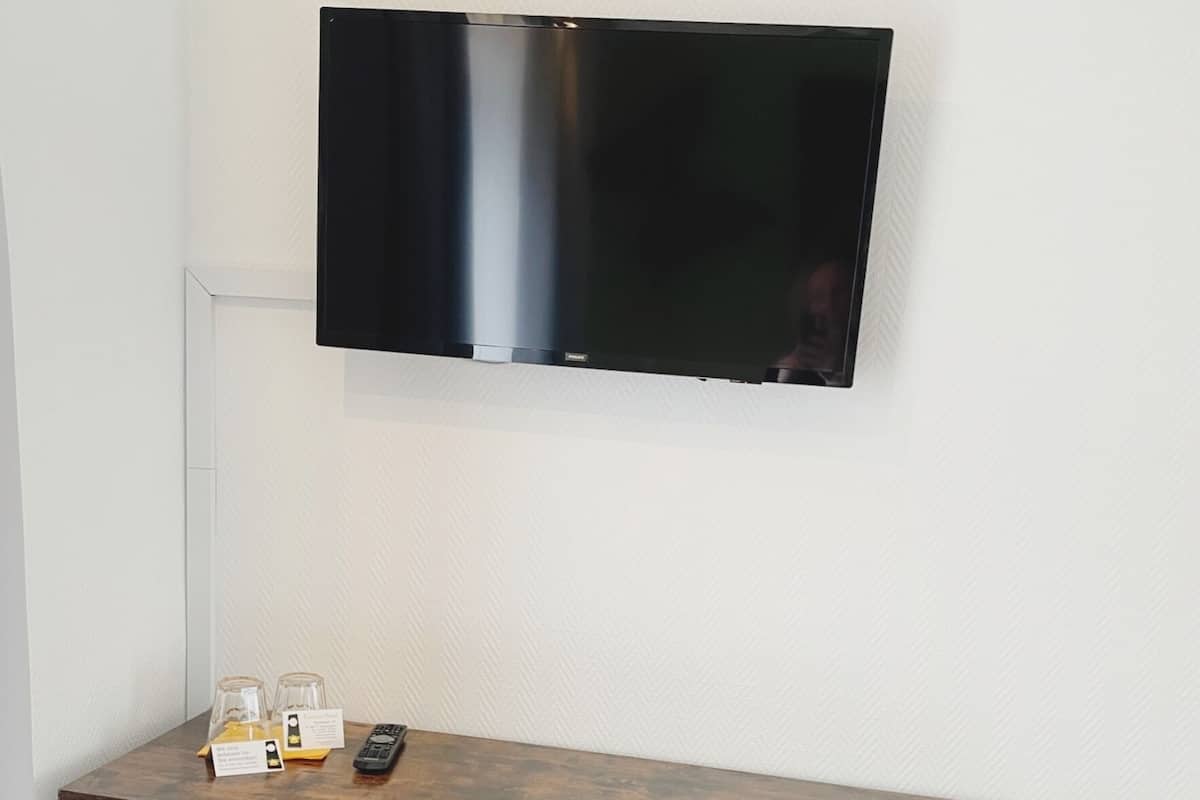 Ett litet arbetsutrymme med en platt-TV som är monterad på väggen, två trästolar och ett litet bord med en fjärrkontroll och en behållare av glas.