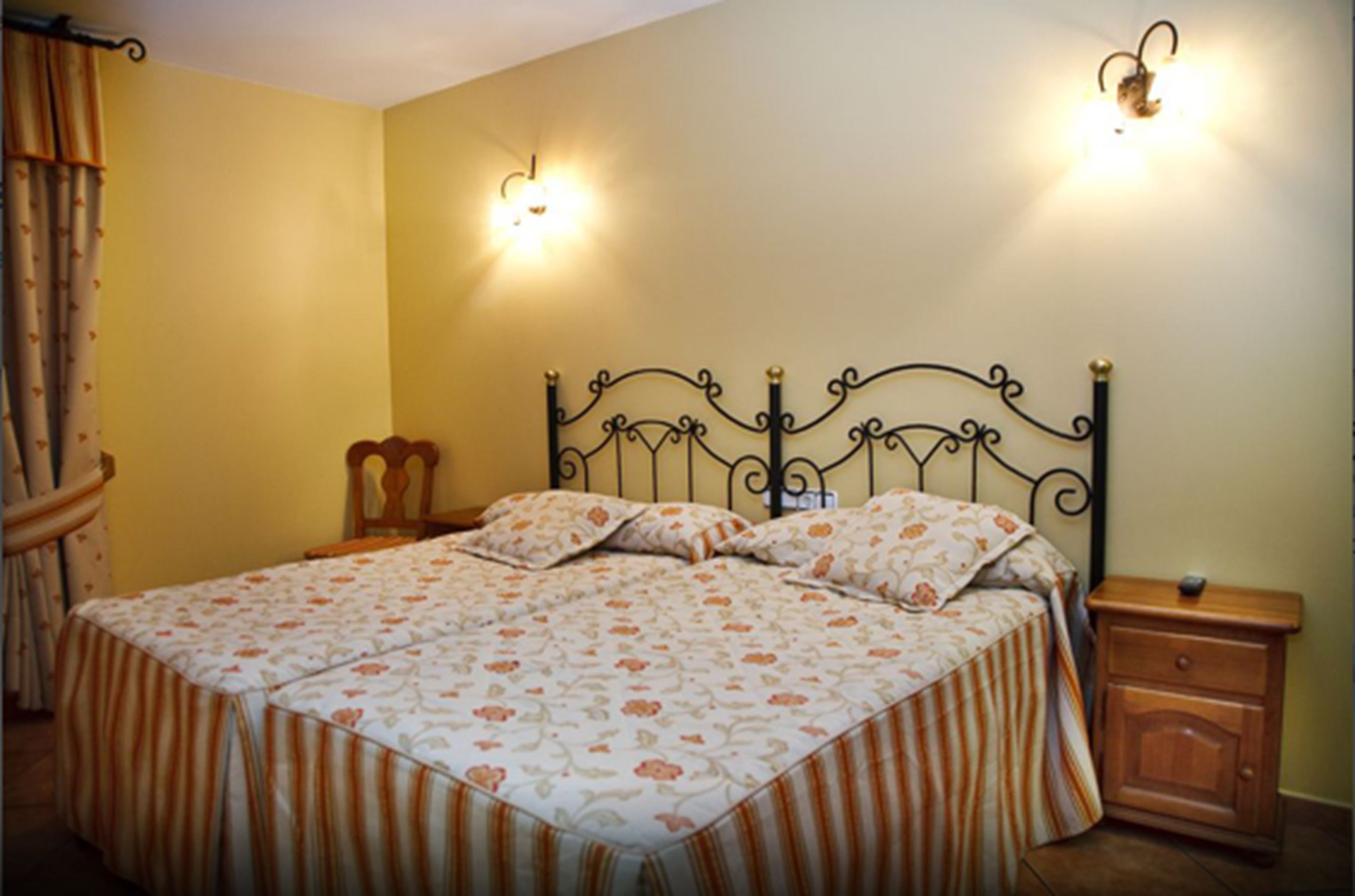 A bedroom with a bed, two wall sconces, a nightstand, and a wooden chair.